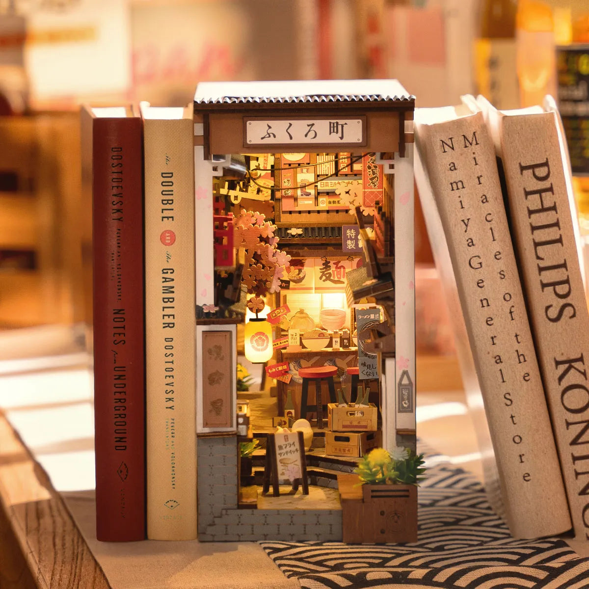 Sakura Wine Alley iluminado entre libros, con faroles y un callejón japonés en miniatura.