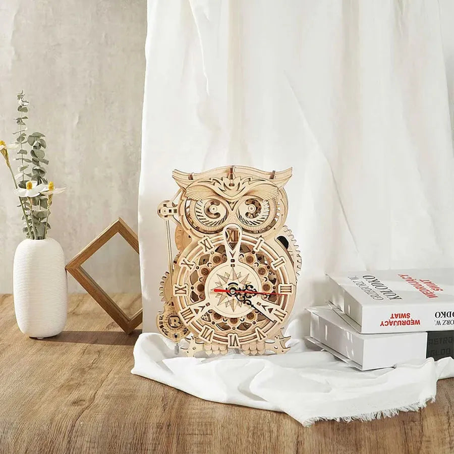Owl Clock sobre una tela blanca junto a libros y un jarrón.