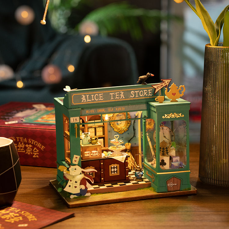 Alice’s Tea Store iluminada sobre una mesa junto a su caja, con luces desenfocadas al fondo