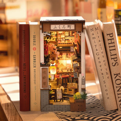 Sakura Wine Alley iluminado entre libros, con faroles y un callejón japonés en miniatura.
