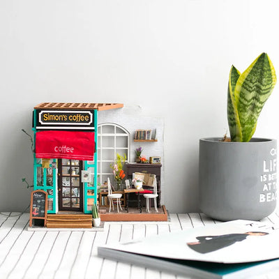 Simon’s Coffee montado sobre una mesa junto a una planta y un cuaderno.