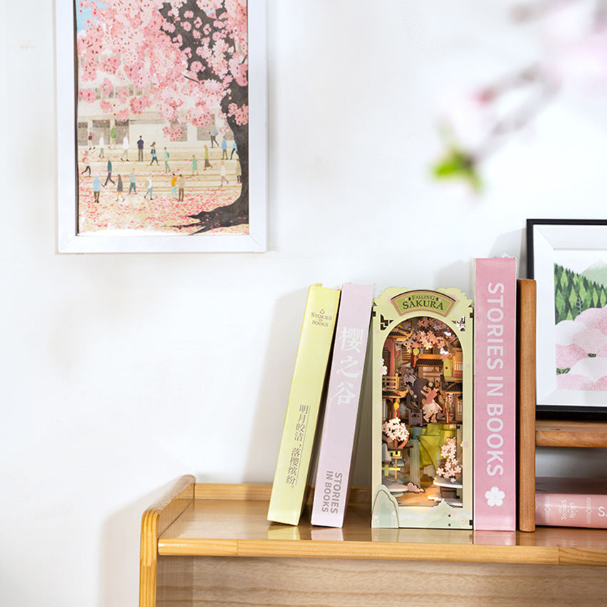 Falling Sakura colocado entre libros en una estantería junto a una lámina de cerezos.