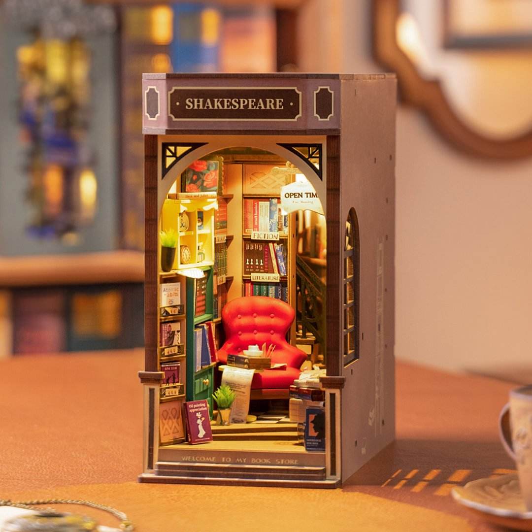 
Shakespeare’s Bookstore iluminado sobre una mesa, con sillón rojo y libros en miniatura.