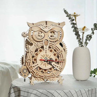 Owl Clock montado sobre una mesa junto a un jarrón con flores.