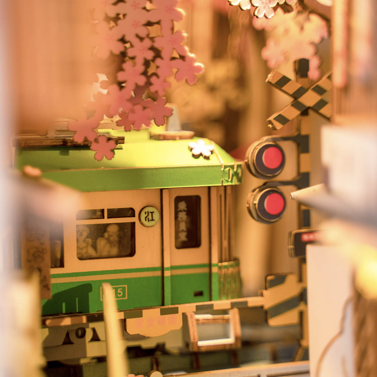
Primer plano del tren verde y la señal ferroviaria de Sakura Densya, bajo las flores de cerezo y con luz cálida.