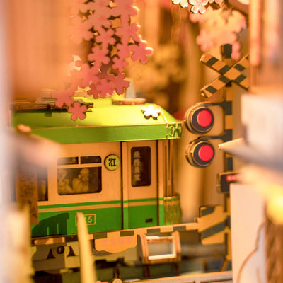 Primer plano del tren verde y la señal ferroviaria de Sakura Densya, bajo las flores de cerezo y con luz cálida.