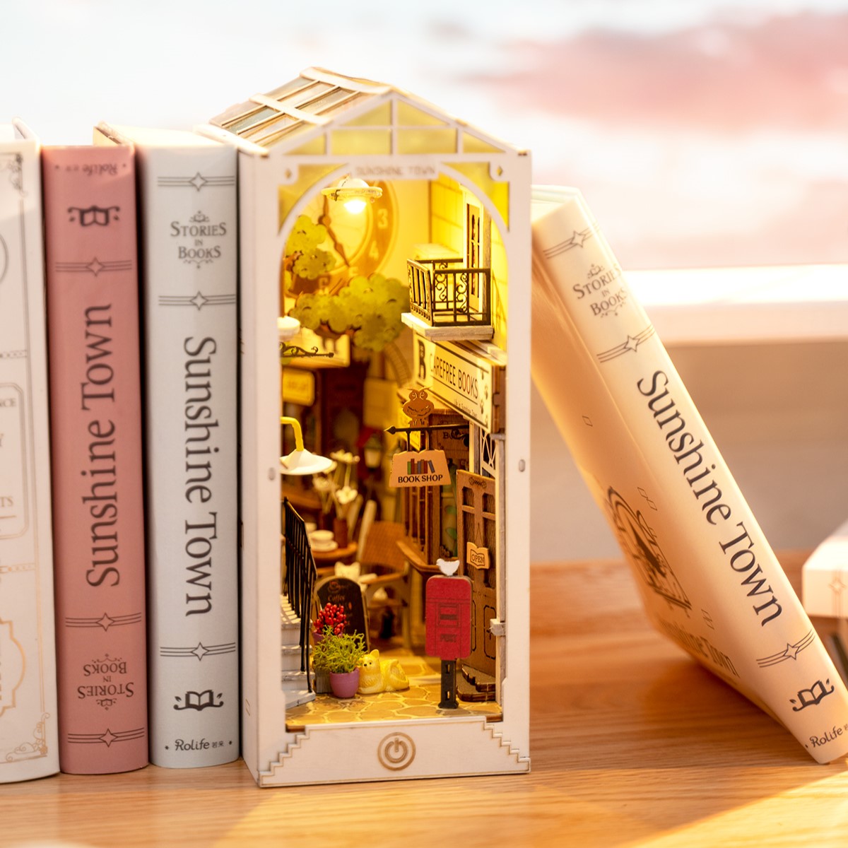 
Sunshine Town iluminado entre libros, con cubierta transparente, balcón y buzón rojo.