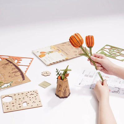 Manos montando los tulipanes naranjas de Orange Tulip junto a paneles e instrucciones.